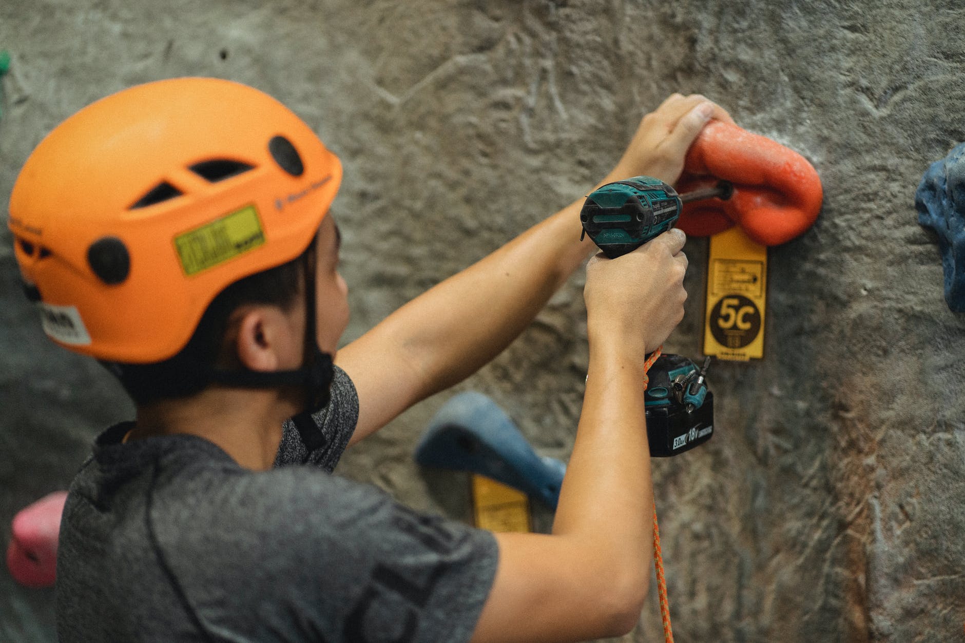 crop athlete fasten climbing hold with screwdriver on wall in gym